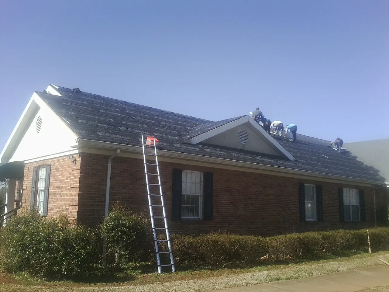 Crew tearing shingles off a brick ranch roof with a ladder set — Metal Roof Repair work by our crew in Walpole
