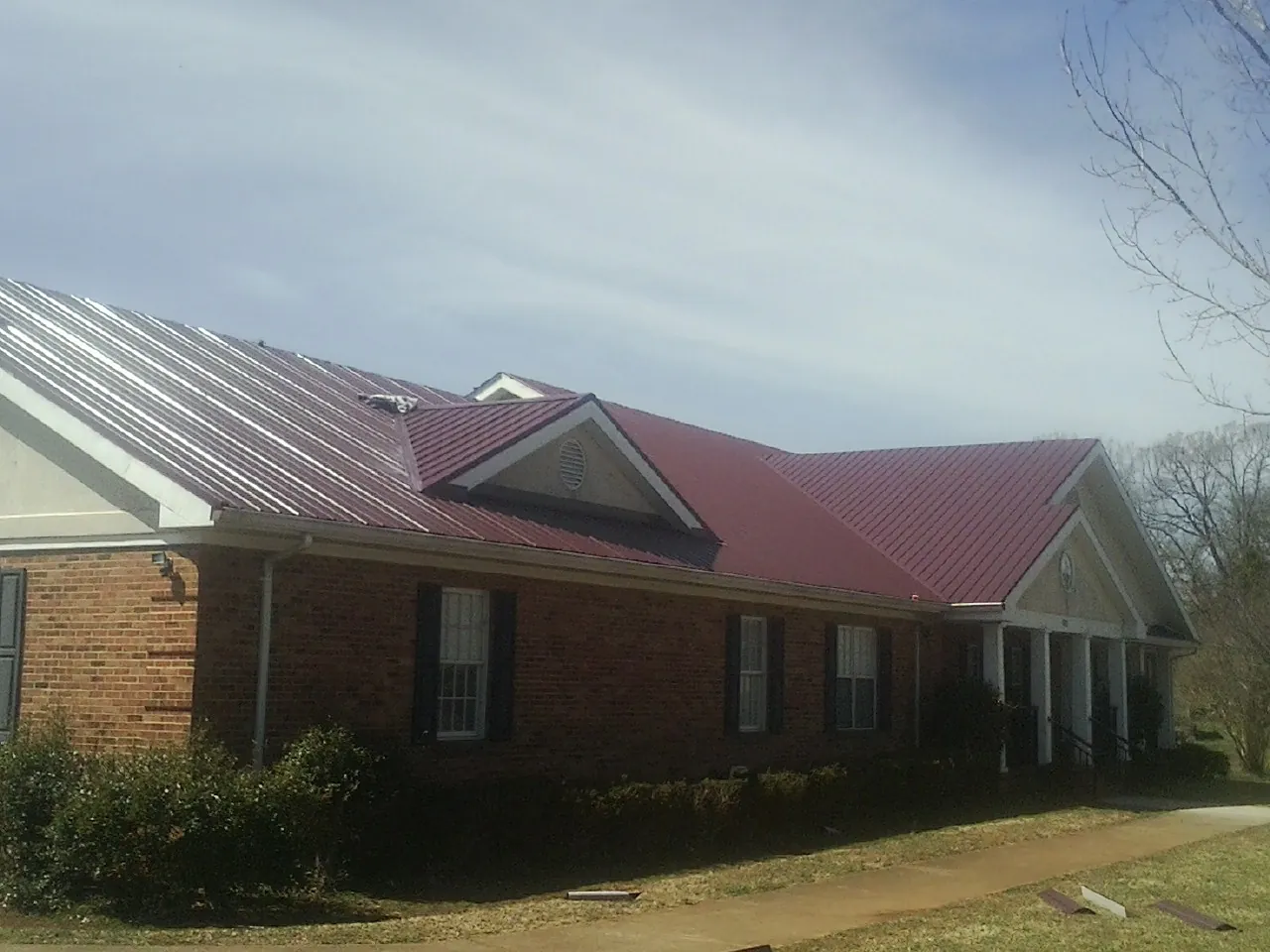 Red metal roof with gabled entries on a long brick building, from a Hail Damage Roof Repair job in Walpole