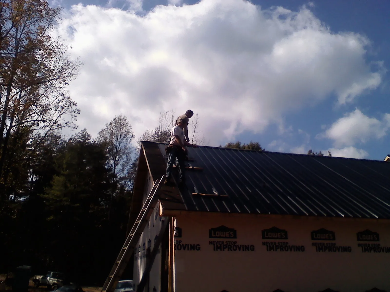 Roofer fastening dark metal panels high against a cloudy sky, from a Roof Inspection job in Walpole