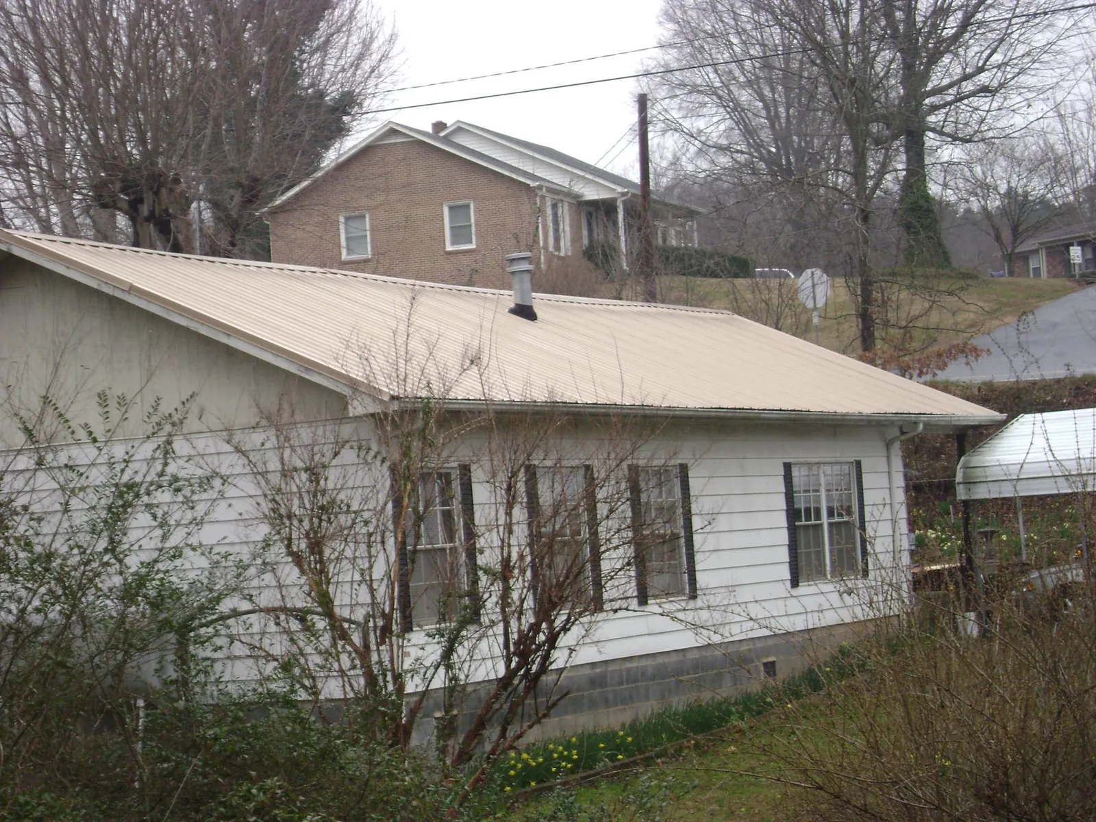 Tan metal roof on a white sided house set into a hillside — Commercial Roofing by Roofing Brothers in Walpole